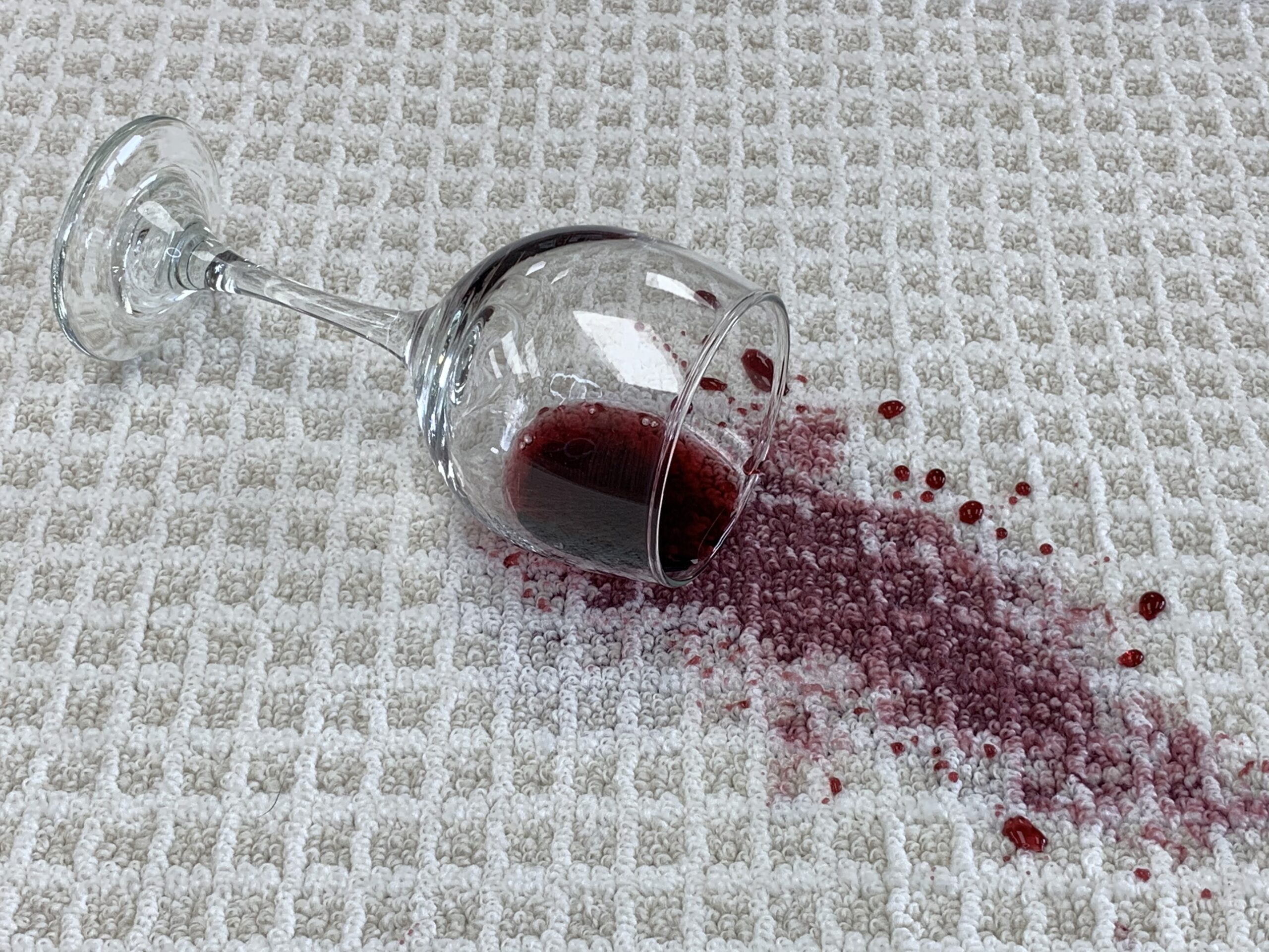 Red wine is splattered across a textured white carpet.