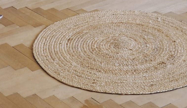 Close up of a jute rug on wood flooring. Jute and other grass rugs do not react well to water or other liquids.  Call a professional for cleaning tips.