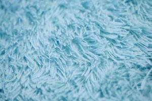 Close up of a light blue shag rug. A shag rug is an example of a high-pile rug that is soft and fluffy but vulnerable to high-traffic damage.