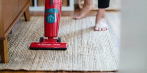 Person uses red bagged vacuum to clean a light area rug.